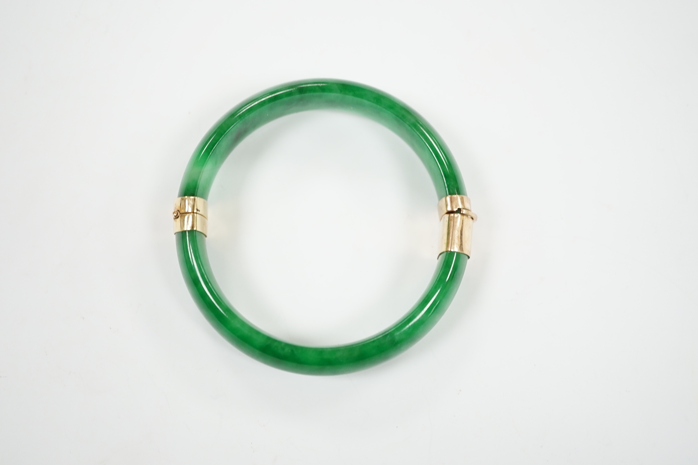 A yellow metal mounted jadeite hinged bangle, interior diameter 58mm, gross weight 59 grams.